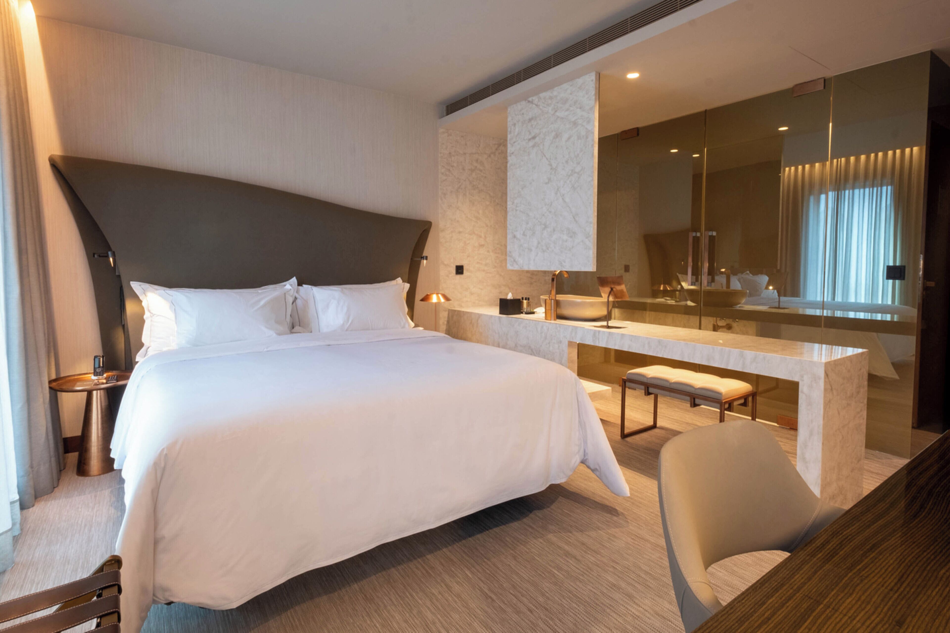 Een moderne hotelkamer met een groot bed, een zithoek met een bank, een bureau en een grote spiegel.