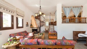A cozy living room with a fireplace, a wooden staircase, and a balcony with curtains.