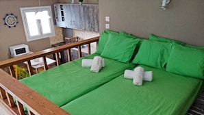 A double bed with green bedding and white towels, a wooden headboard, a small window, and a microwave on the wall.