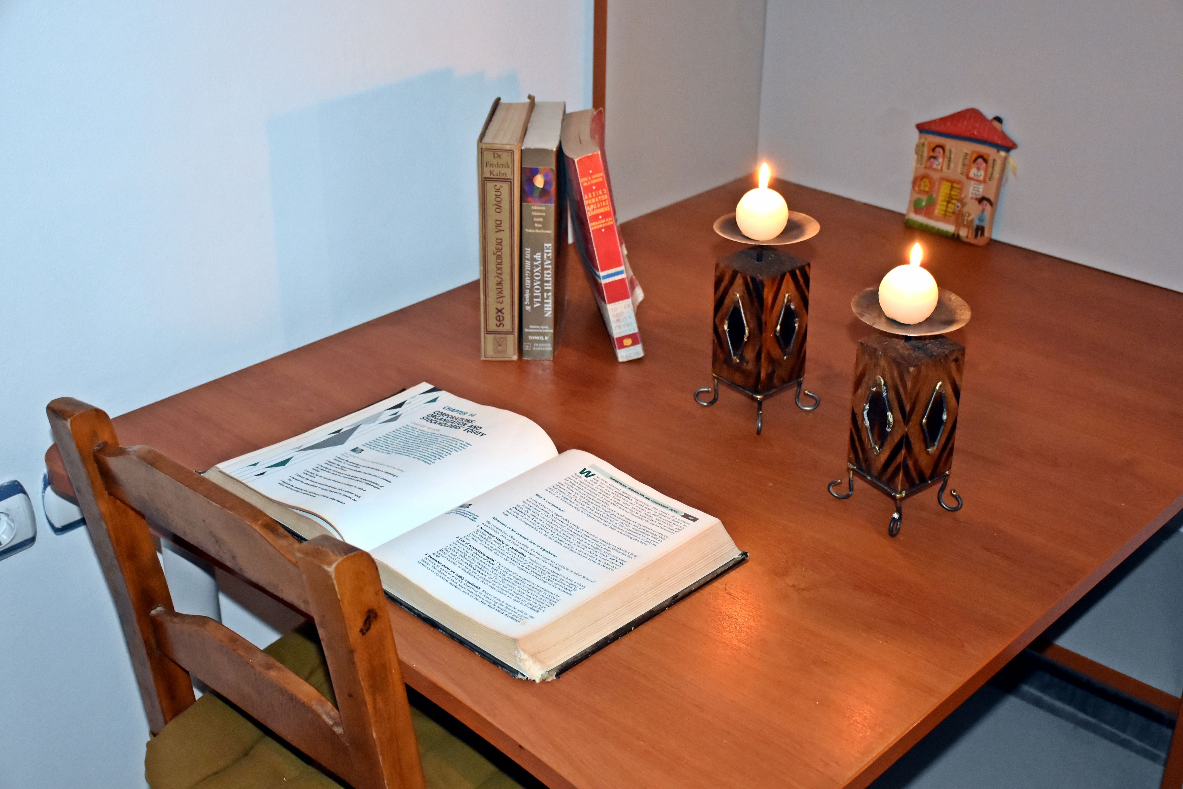 Une table en bois sur laquelle se trouve un livre ouvert, deux bougies et plusieurs livres empilés.