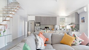A modern living room with a grey sofa, a glass coffee table, and a staircase with wooden steps. - Naomi By Stay Amazing (Cape Town)