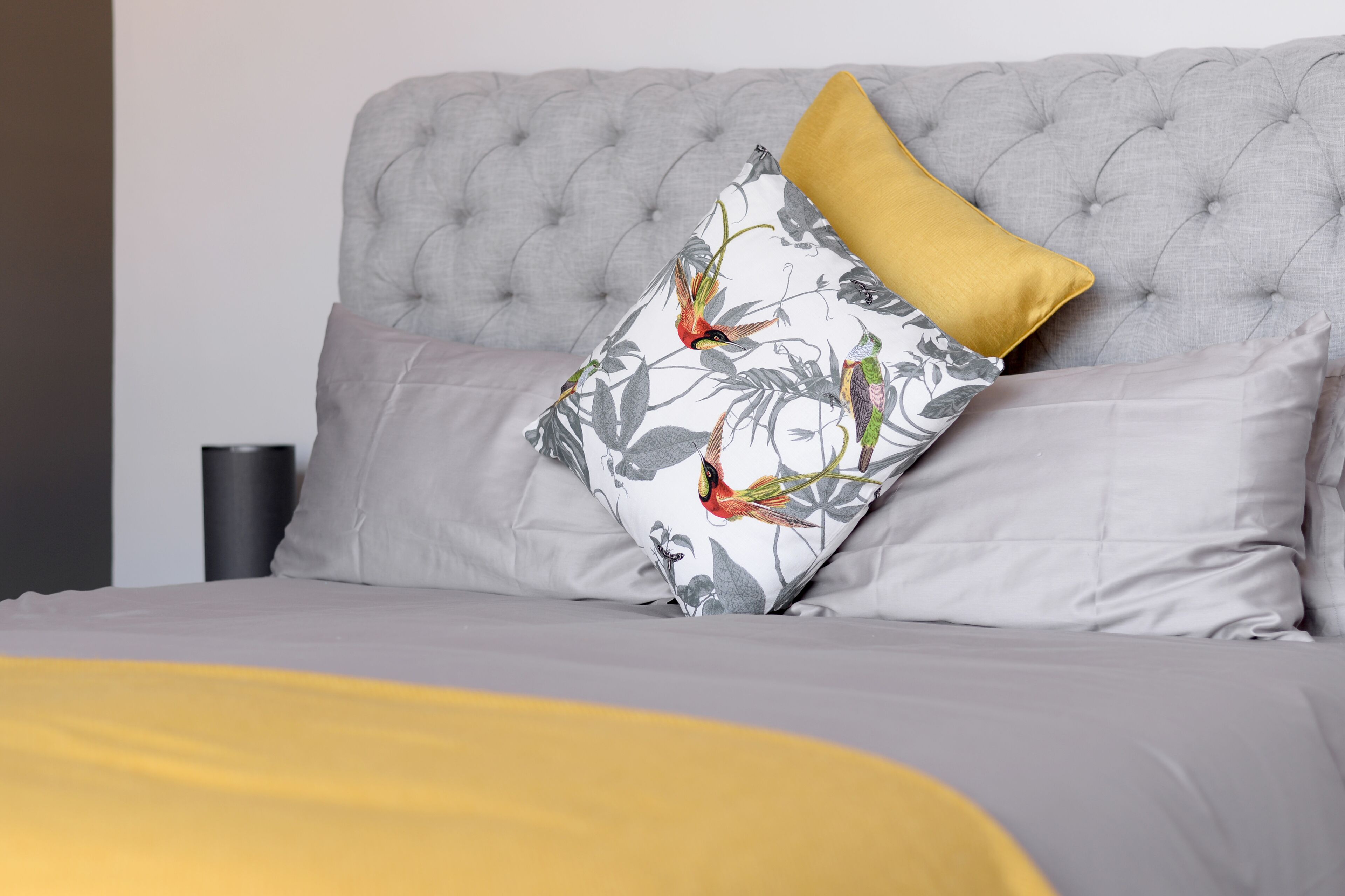 A bed with a tufted headboard, a floral pillow, and a mustard-colored throw blanket.