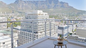 A balcony with a potted plant, overlooking a cityscape with modern buildings and a prominent mountain in the background. - Naomi By Stay Amazing (Cape Town)