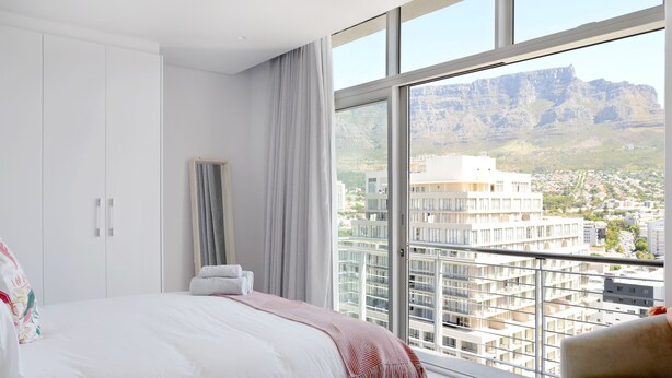 A bedroom with a large bed, a view of a cityscape and mountains through a large window. - Naomi By Stay Amazing (Cape Town)