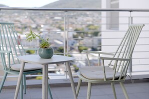 A balcony with a table and two chairs, a potted plant, and a view of a cityscape. - Naomi By Stay Amazing (Cape Town)