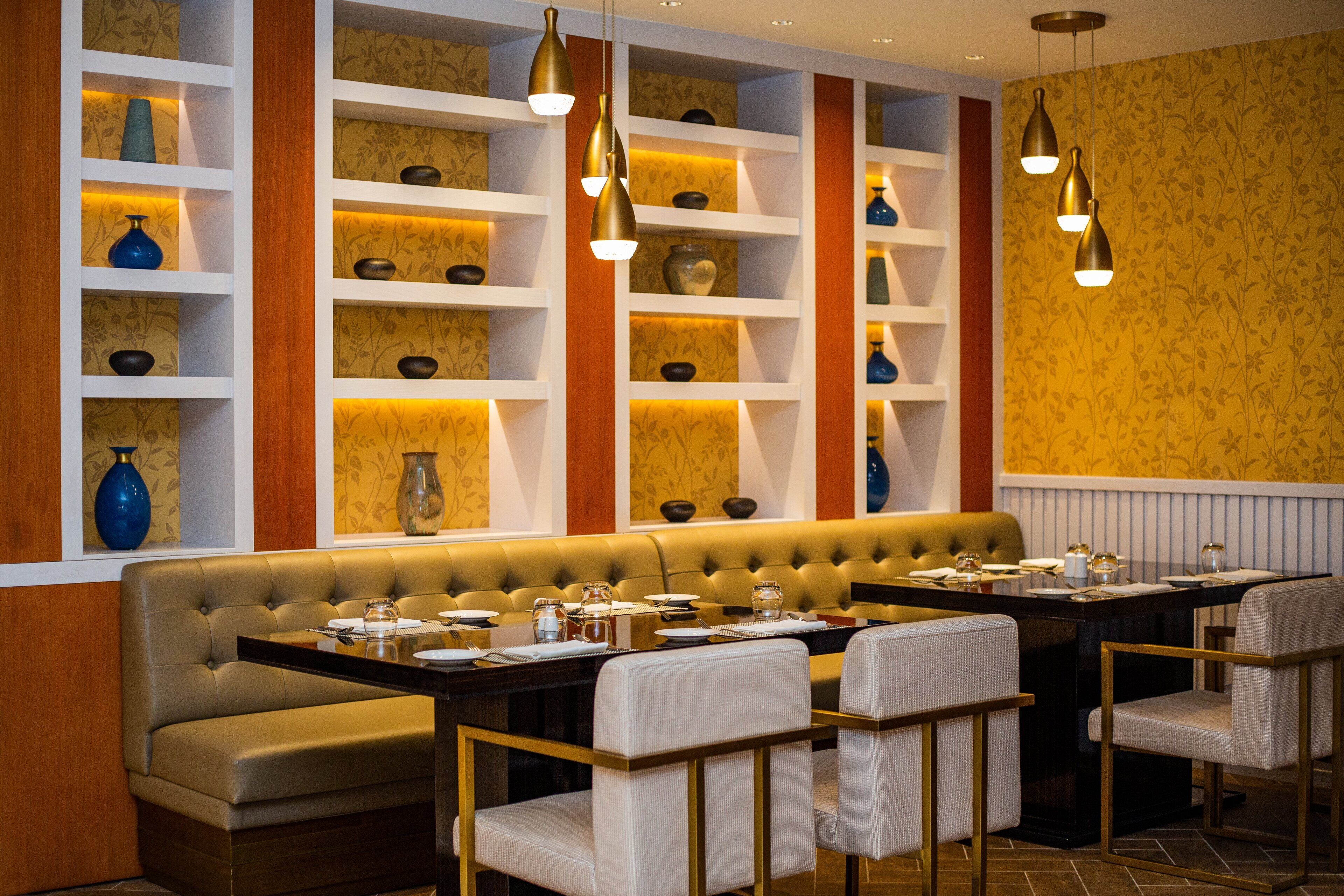 Un restaurante con una amplia zona de asientos tipo banqueta, varios estantes con adornos y lámparas colgantes.