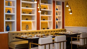 Un restaurante con una amplia zona de asientos tipo banqueta, varios estantes con adornos y lámparas colgantes.