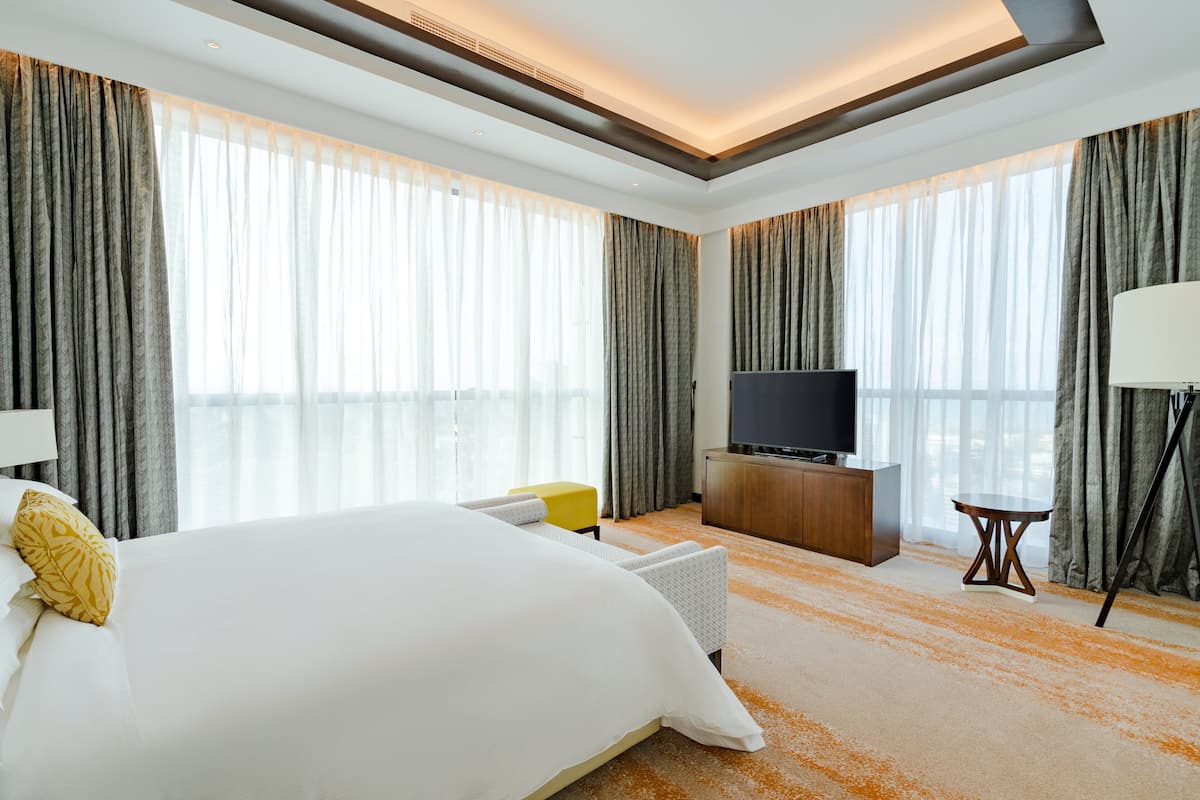 A modern hotel room with a large bed, a flat-screen TV, a small table, and a lamp.