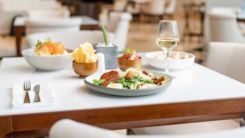 Una mesa de comedor con una ensalada, una copa de vino blanco y diferentes acompañamientos.