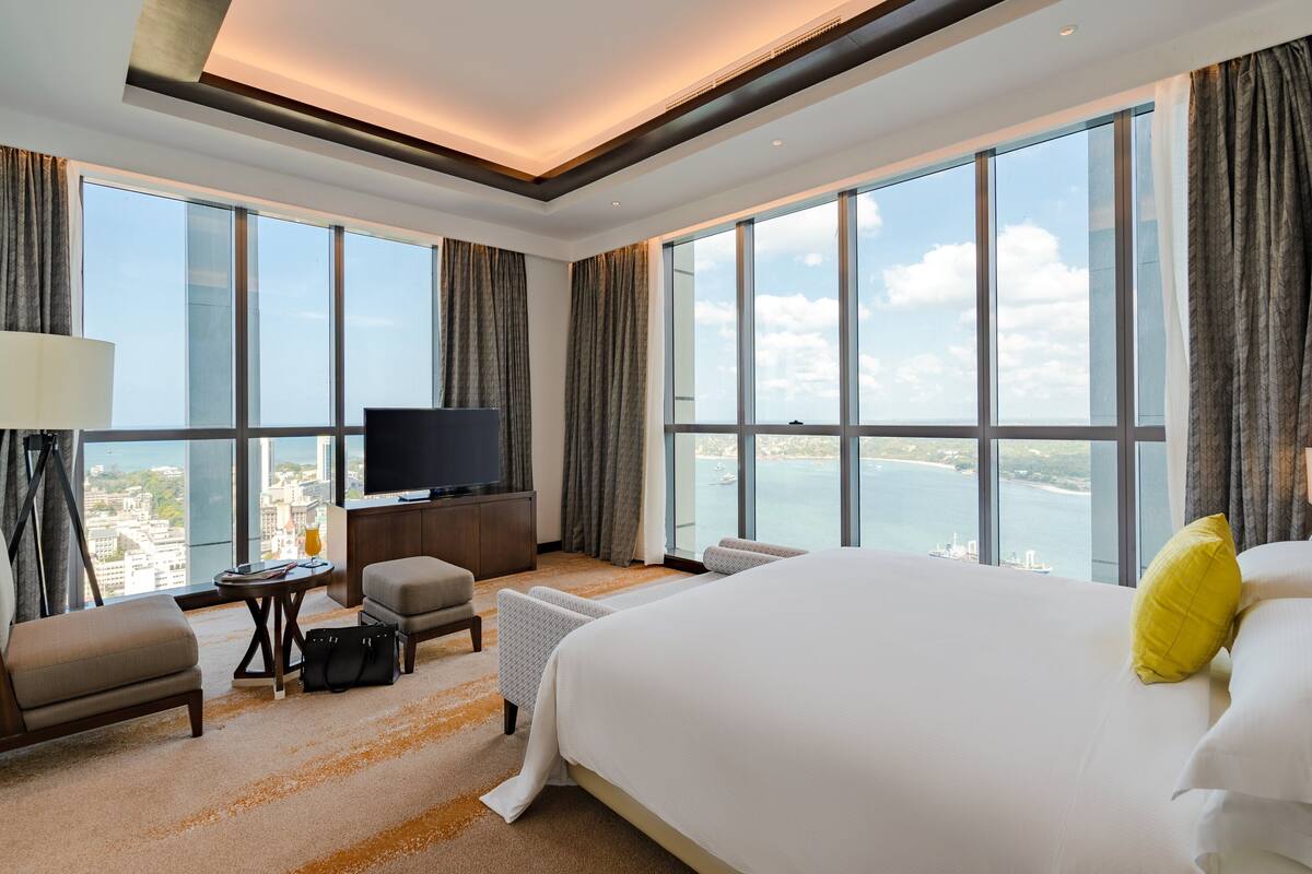A hotel room with a large bed, a TV, a desk, and a view of the sea.