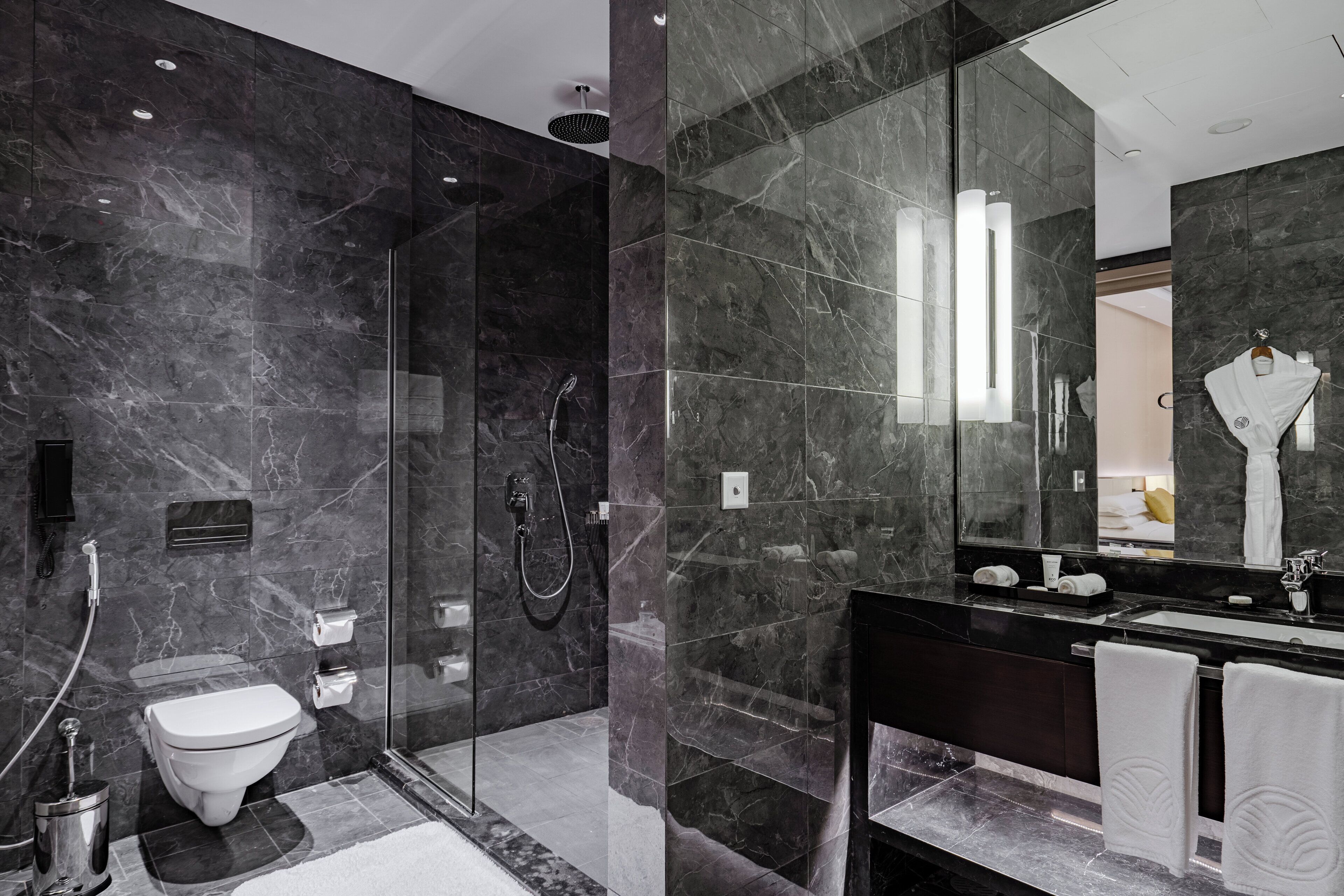 Un baño moderno con ducha de vidrio, inodoro y un espejo grande sobre el lavabo.