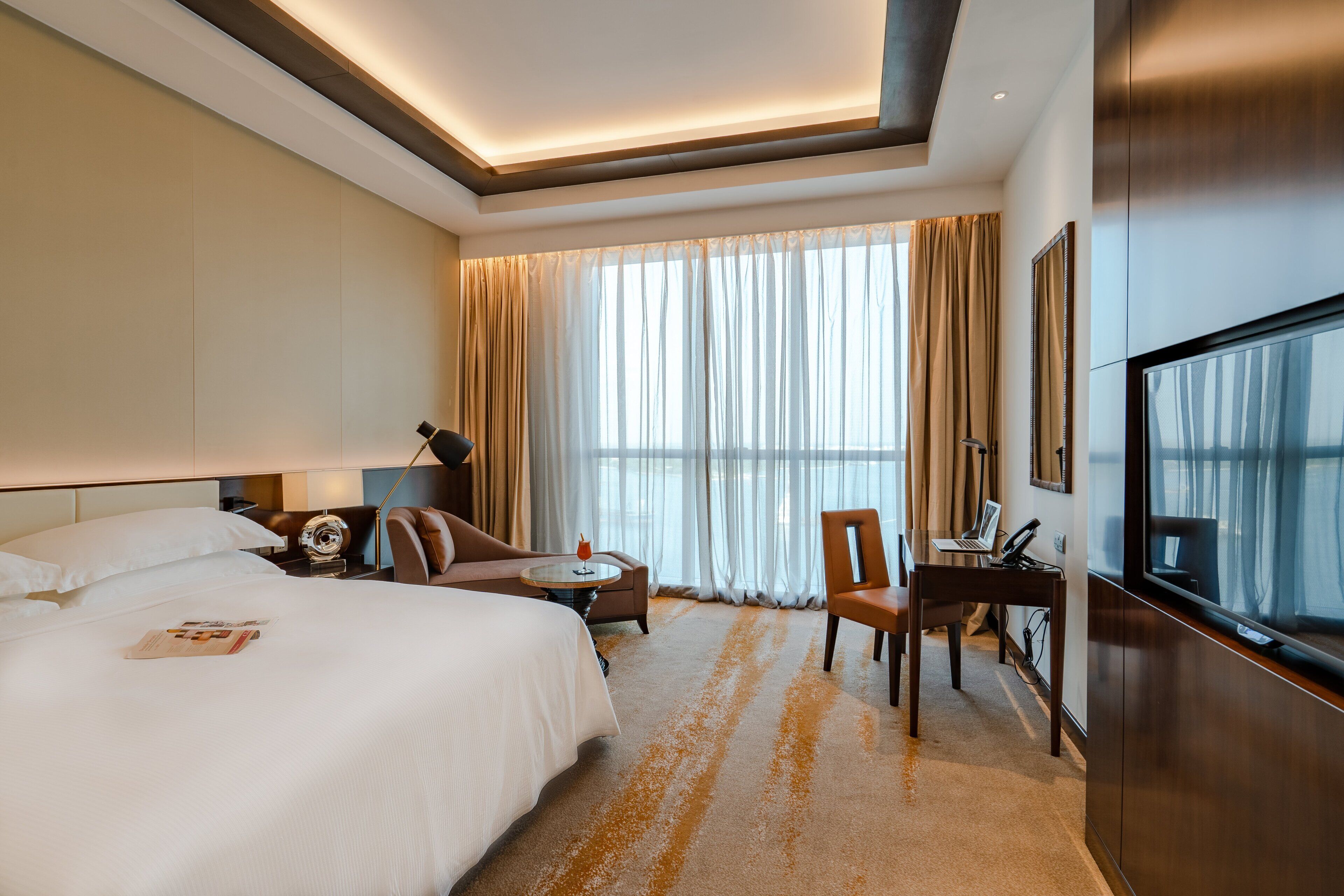 A hotel room with a large bed, a desk with a laptop, a chair, and a TV.