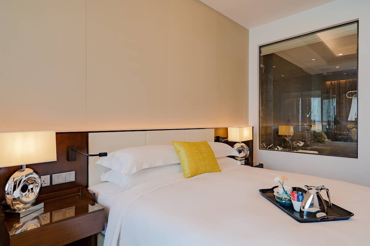 A hotel room with a large bed, bedside lamps, a tray with toiletries, and a mirror reflecting the room.
