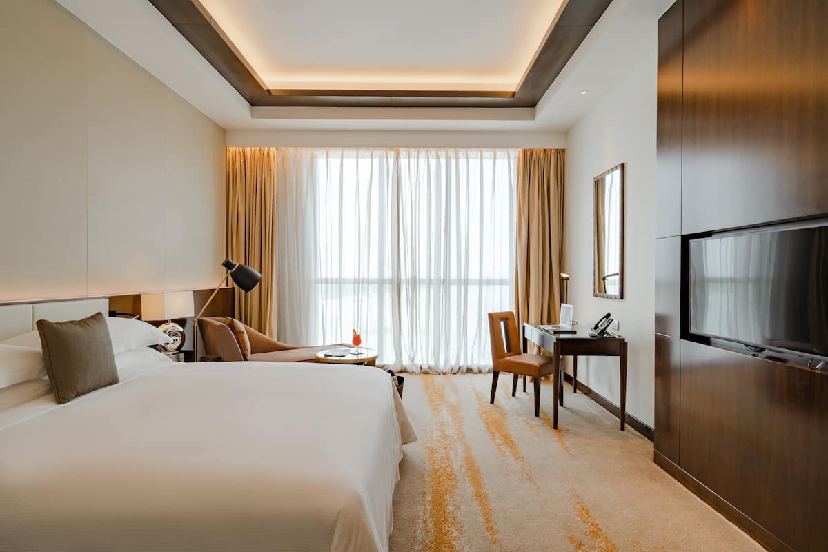 A hotel room with a large bed, a desk, a chair, a TV, and a window with curtains.