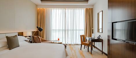 Habitación de hotel con una cama grande, un escritorio, una silla, un televisor y una ventana con cortinas.