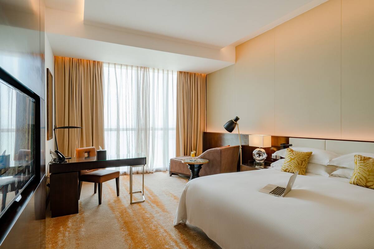 A hotel room with a bed, desk, chair, and a TV.