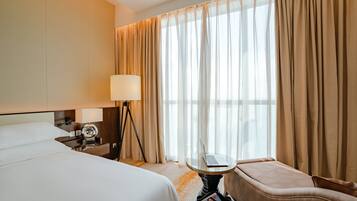 A hotel room with a bed, a desk with a laptop, a lamp, and a chair.