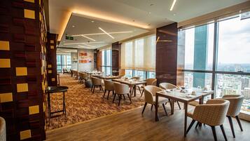 A modern dining area with tables and chairs, large windows offering a city view, and a patterned wall.