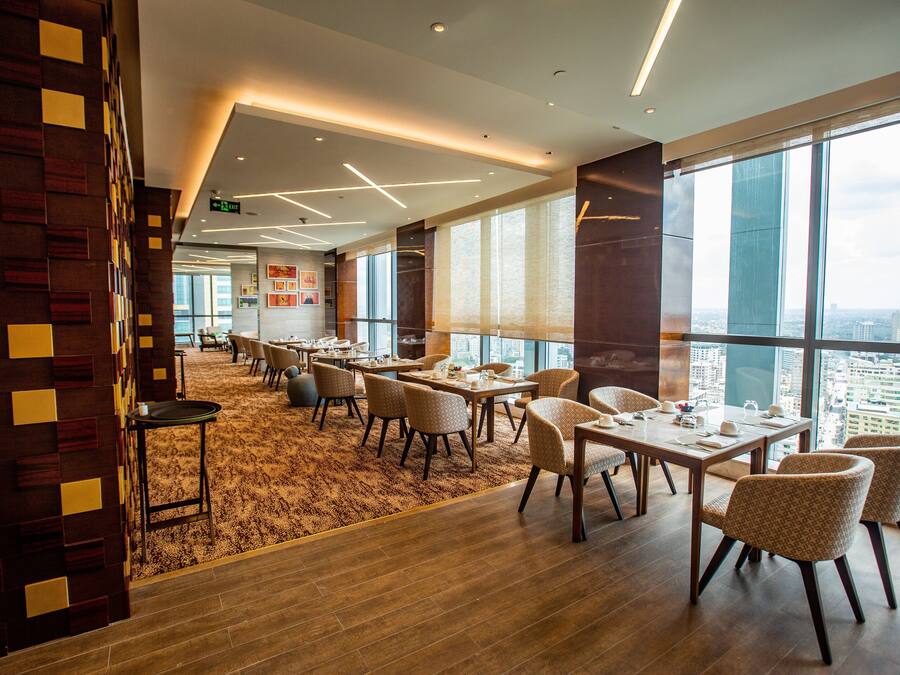 A modern dining area with tables and chairs, large windows offering a city view, and a patterned wall.
