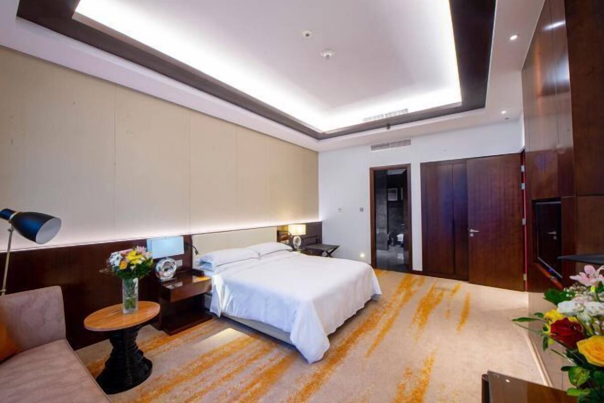 A modern hotel room with a bed, bedside table, lamp, and a view of the hallway.