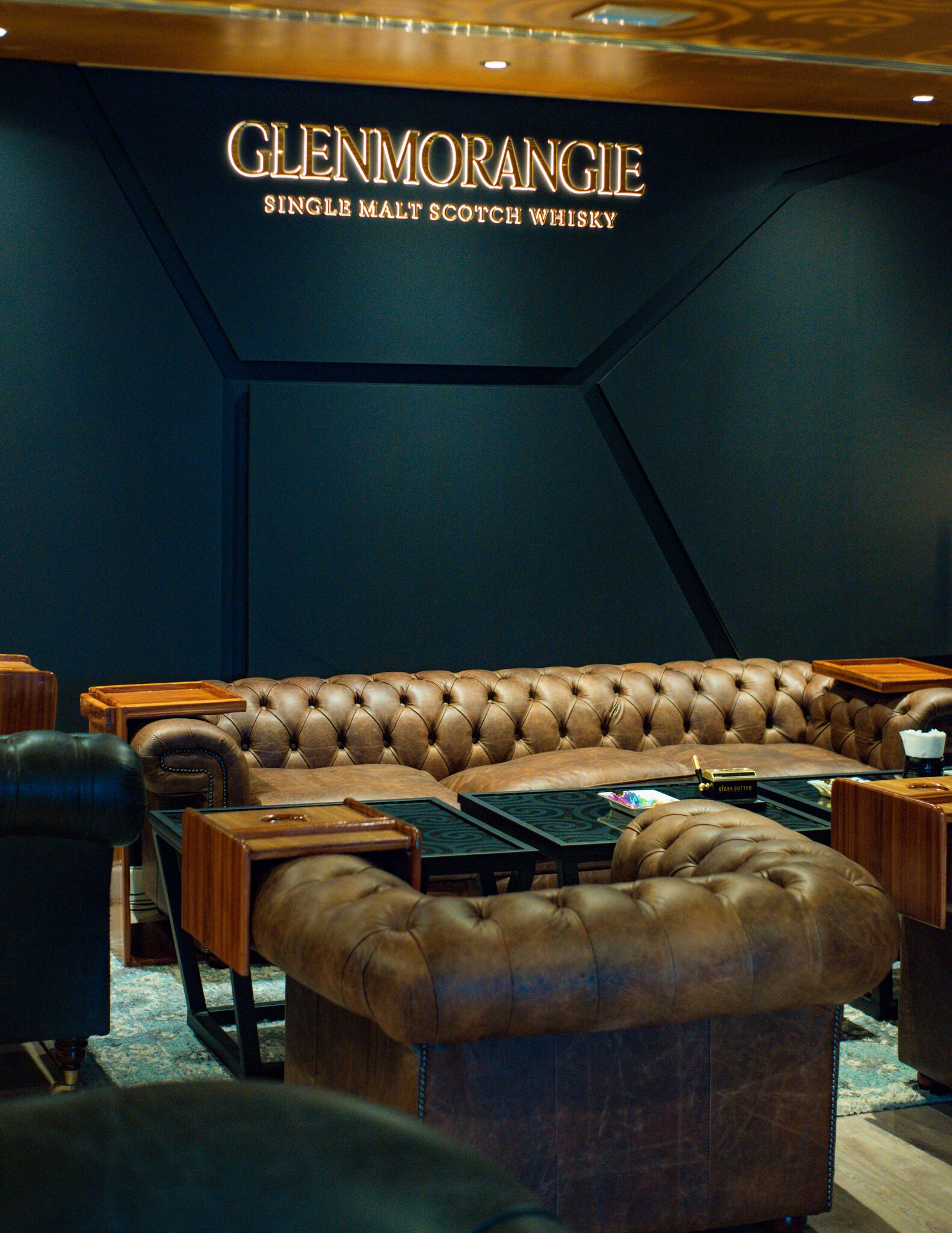A luxurious lounge area with a leather sofa, wooden side tables, and a sign for Glenmorangie Single Malt Scotch Whisky.
