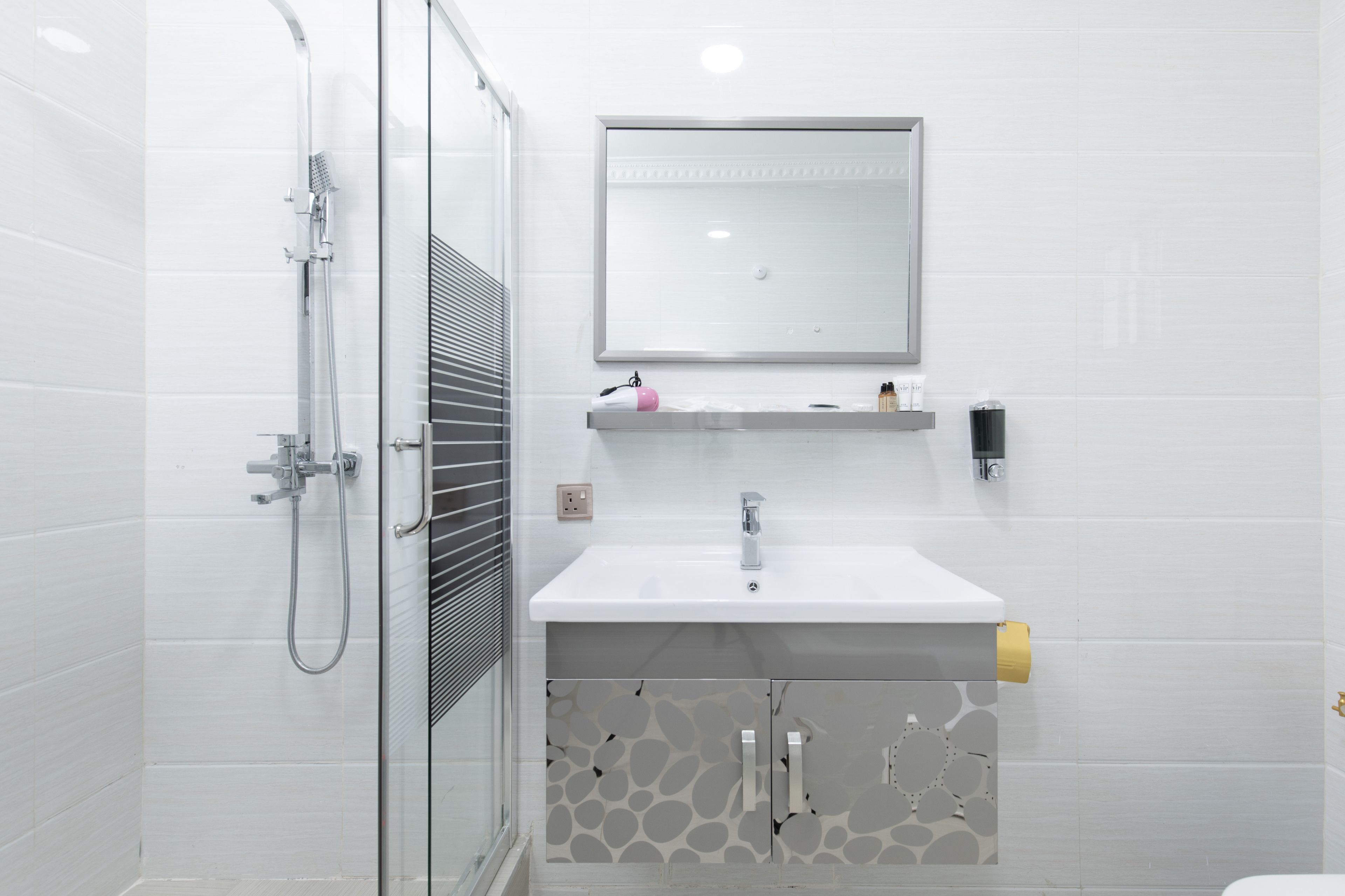 A modern bathroom with a glass shower enclosure, a white sink with a mirror above it, and a patterned cabinet below.