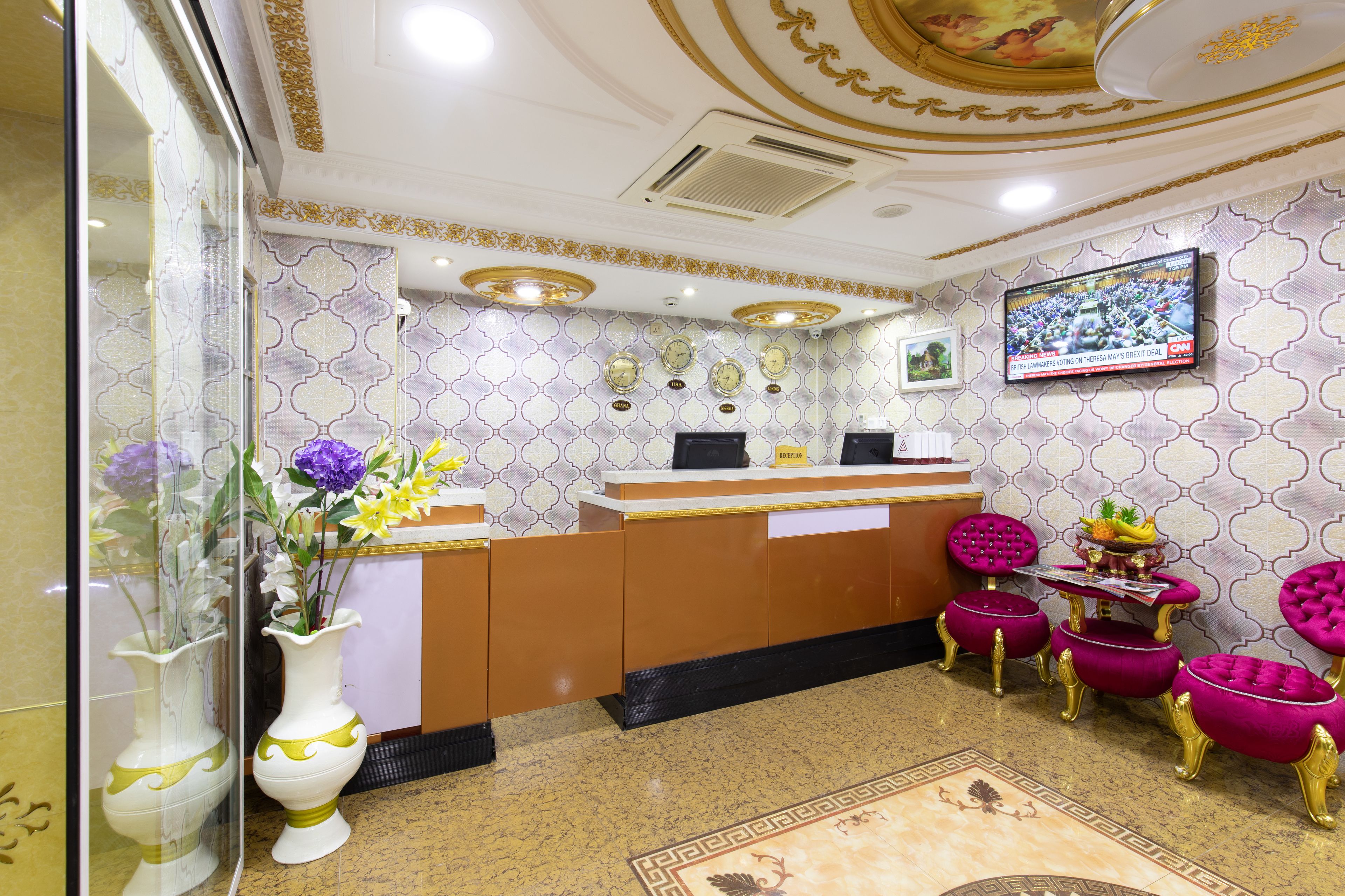 A reception area with a counter, a television mounted on the wall, and a decorative vase with flowers.