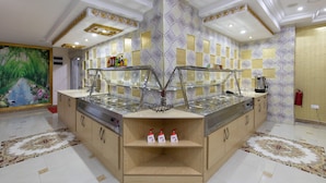 A modern kitchen with a central island, a painting on the left, and patterned wallpaper. - AG Hotel and Suites (Accra)