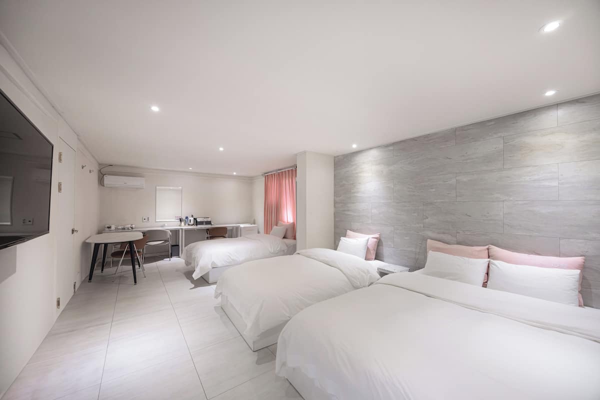 A modern hotel room with two beds, a desk, and a shower area.