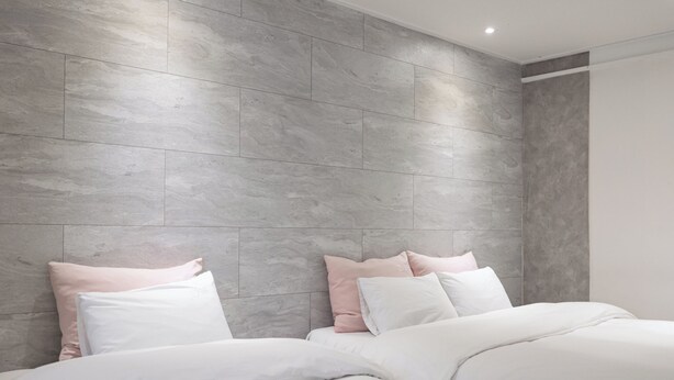 Une chambre à coucher moderne avec une tête de lit carrelée de couleur grise, du linge de lit blanc et une palette de couleurs neutres.