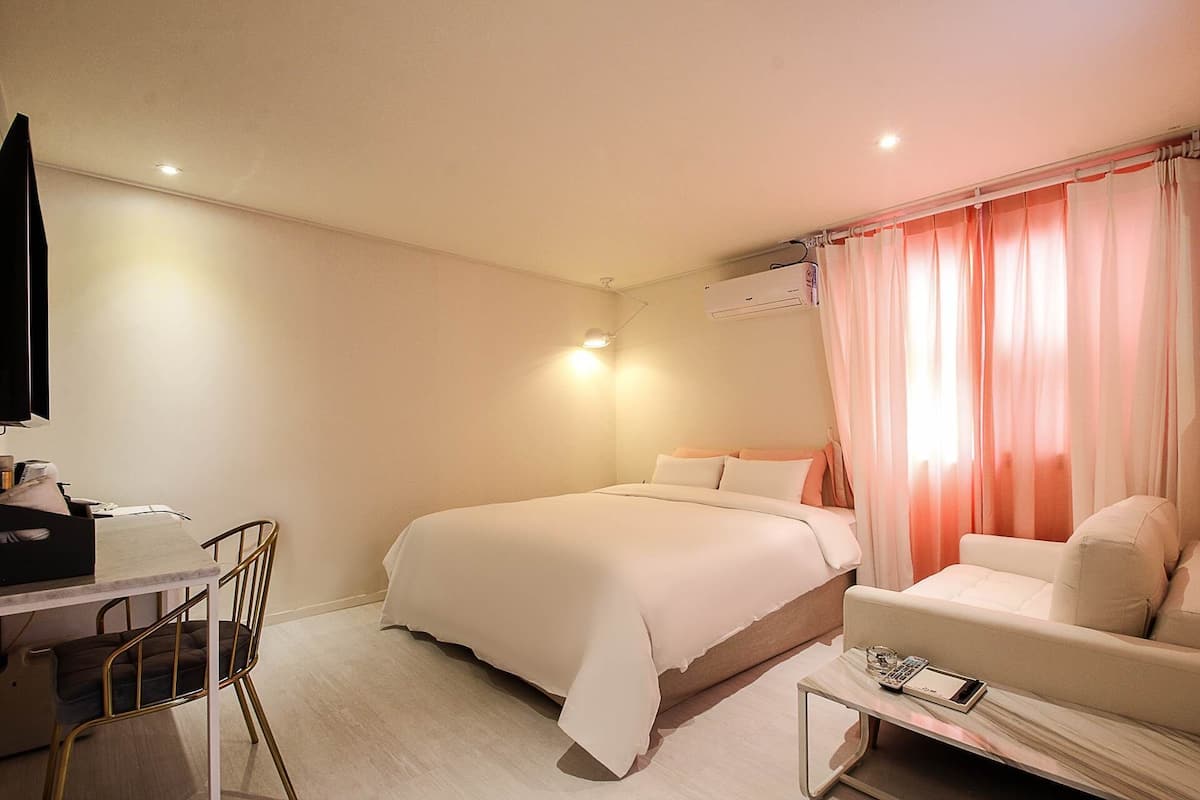 A hotel room with a bed, a desk, a chair, and a small table.