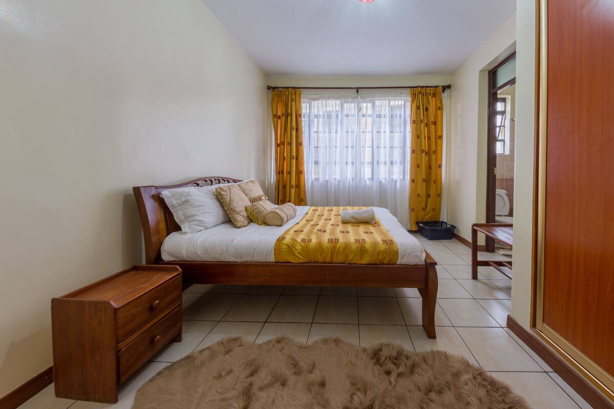 Un dormitorio con una cama de madera, una mesita de noche, un tapete mullido y una ventana con cortinas.
