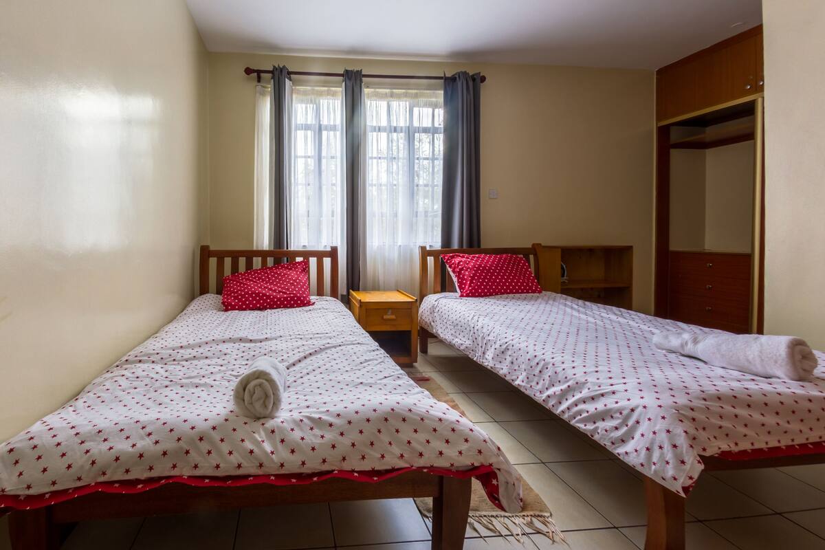 Una habitación con dos camas individuales, un armario de madera, una mesita de noche pequeña y una ventana con cortinas.