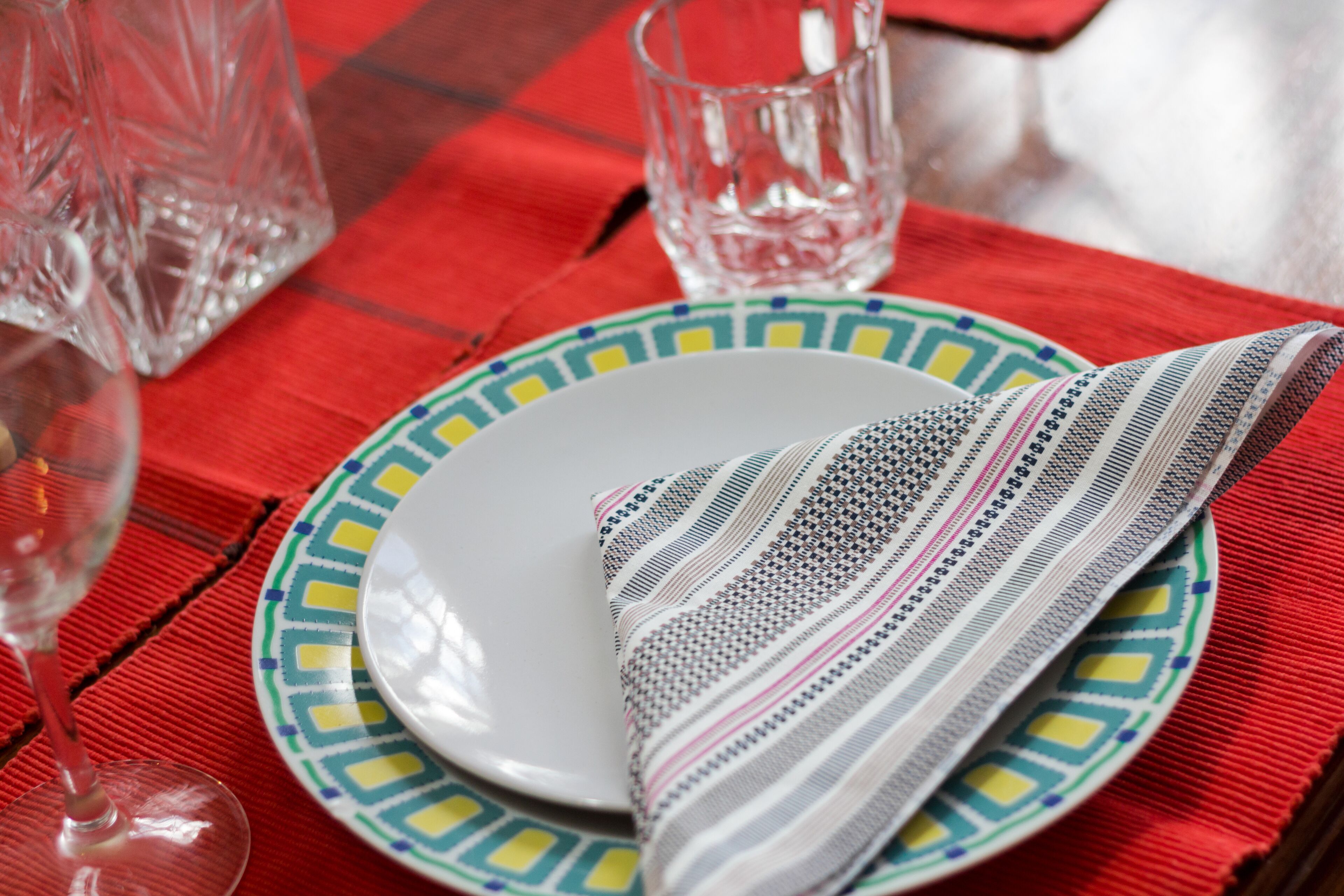 A table setting with a white plate, a colorful patterned napkin, and a clear glass.