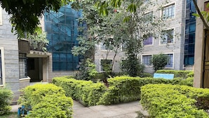 Un patio con un sendero de piedra, setos bien cuidados y un edificio con ventanas grandes y fachada de vidrio.