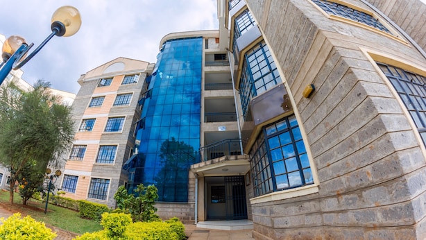 Un edificio de varios pisos con fachada de vidrio moderna, exterior de piedra y un jardín bien cuidado.