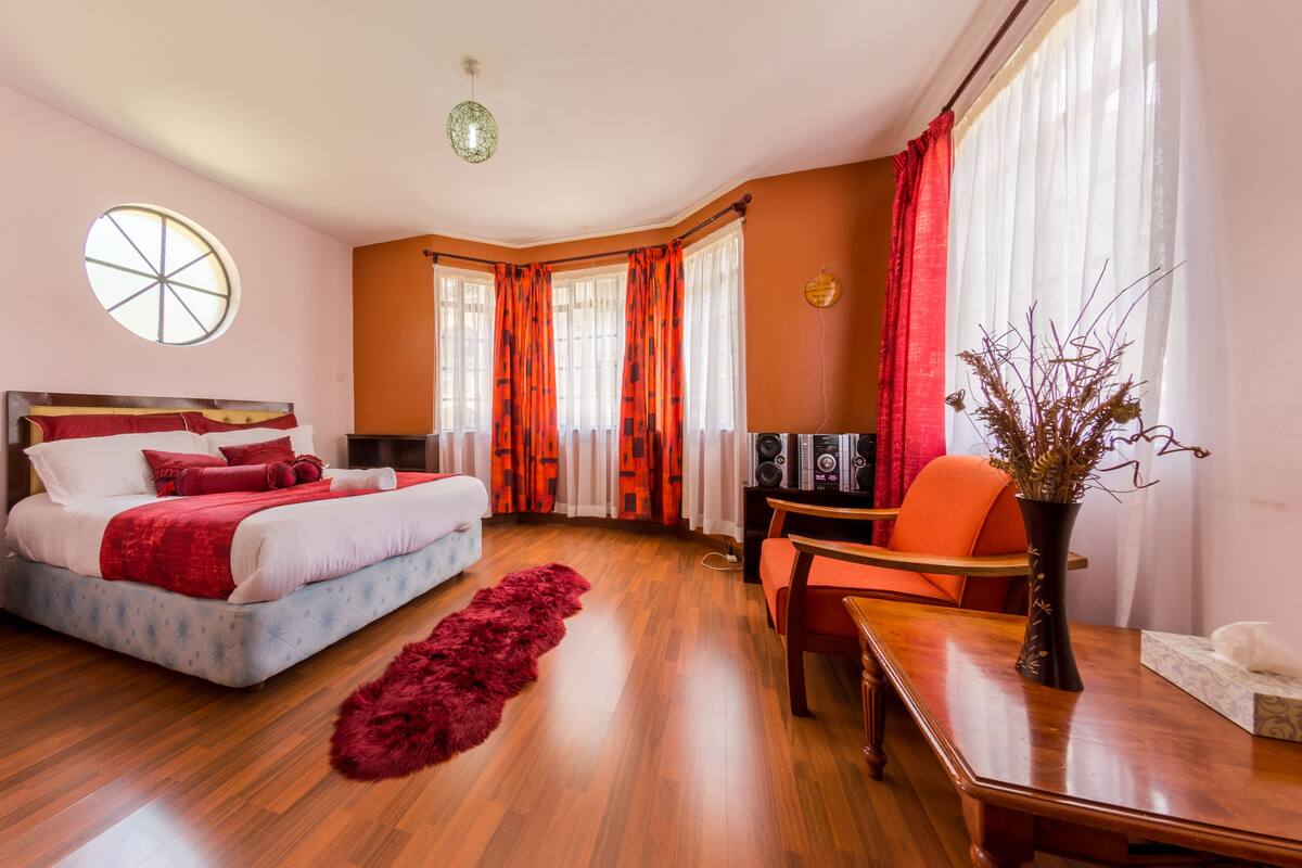 Un dormitorio con cama, escritorio, silla, alfombra roja y ventana con cortinas.