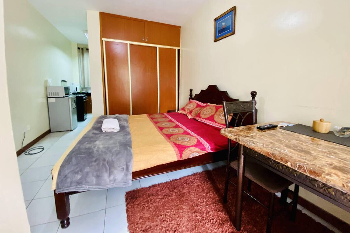 Un dormitorio con cama, escritorio, silla, mesita, microondas y refrigerador.