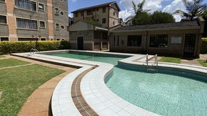 Una piscina de diseño curvo, rodeada por un césped cuidado y un edificio con varias ventanas y tejado de baldosas.