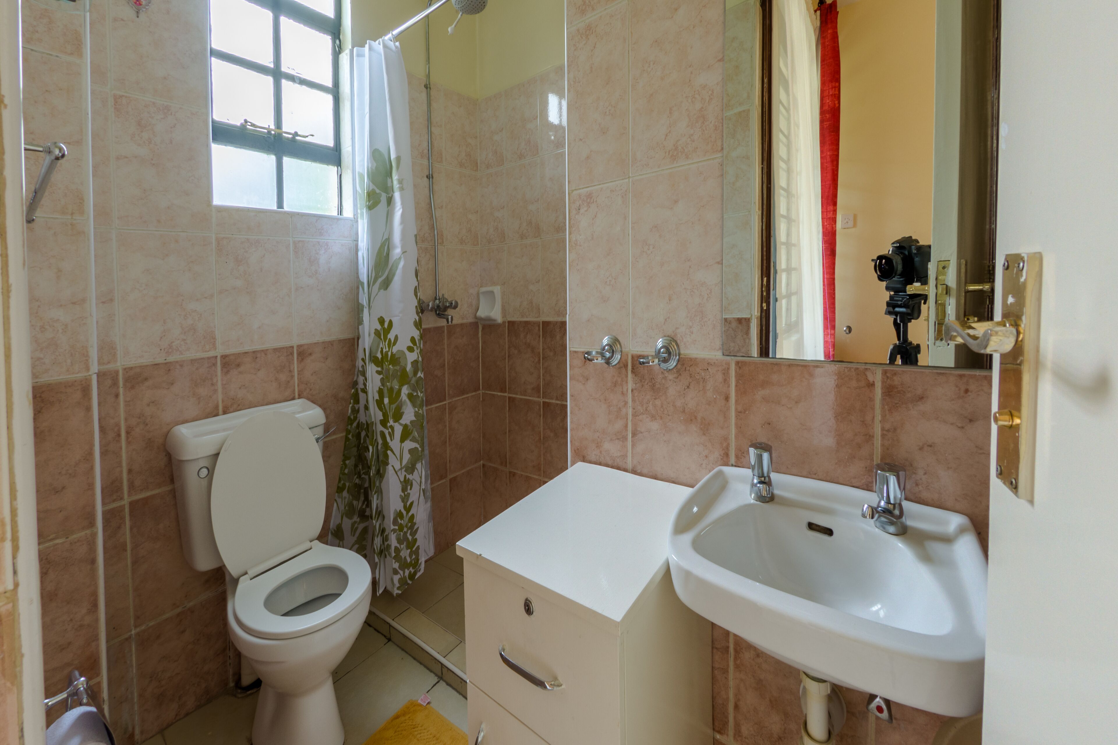 A bathroom with a toilet, shower, sink, and a mirror.