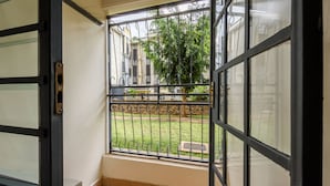 Un balcón con barandilla de metal, vistas a un espacio verde y un edificio al fondo.