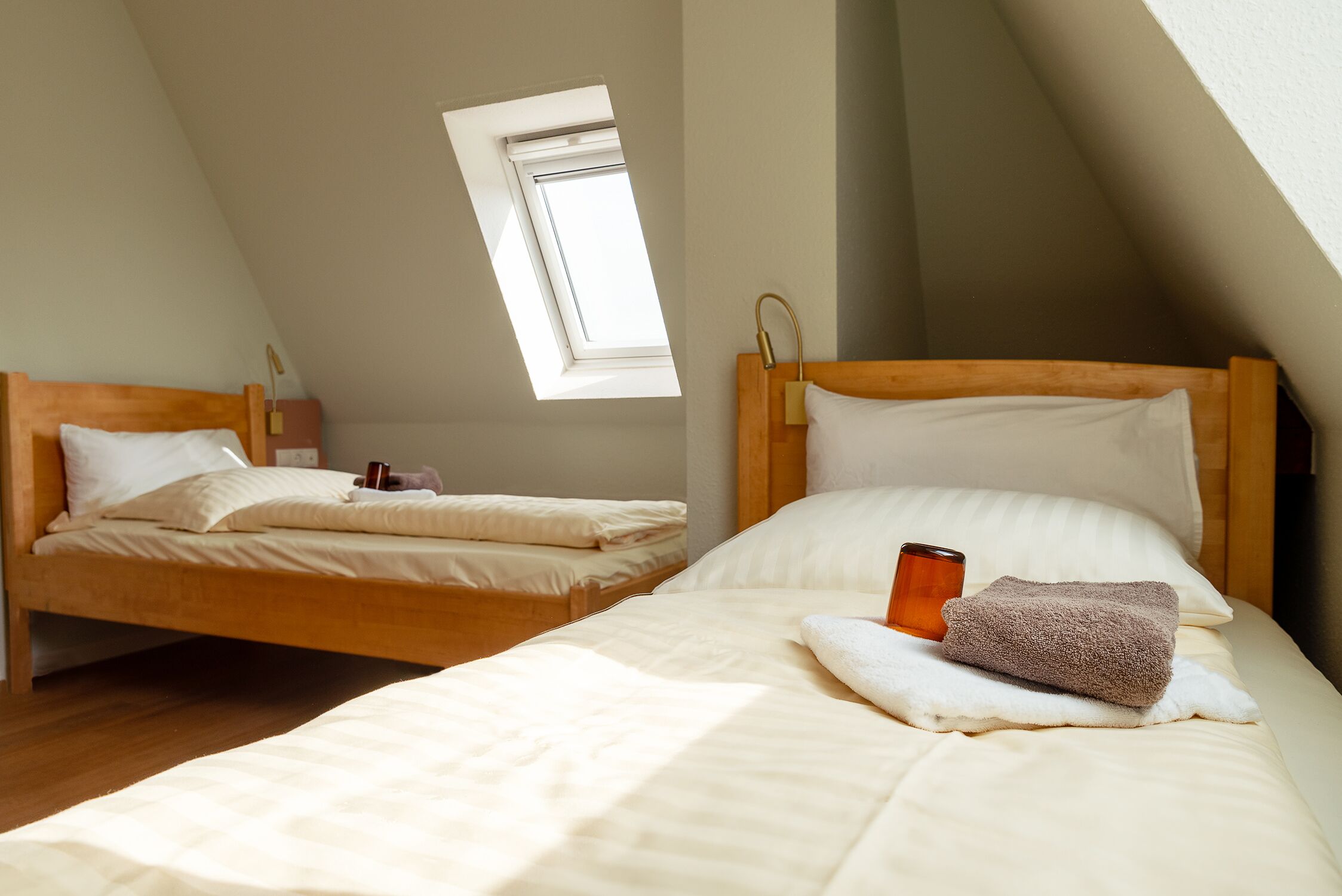 A room with two beds, a skylight, and a wooden headboard.