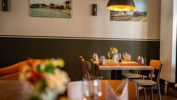Un comedor con una mesa dispuesta para dos, sillas, un jarrón con flores y dos cuadros en la pared.