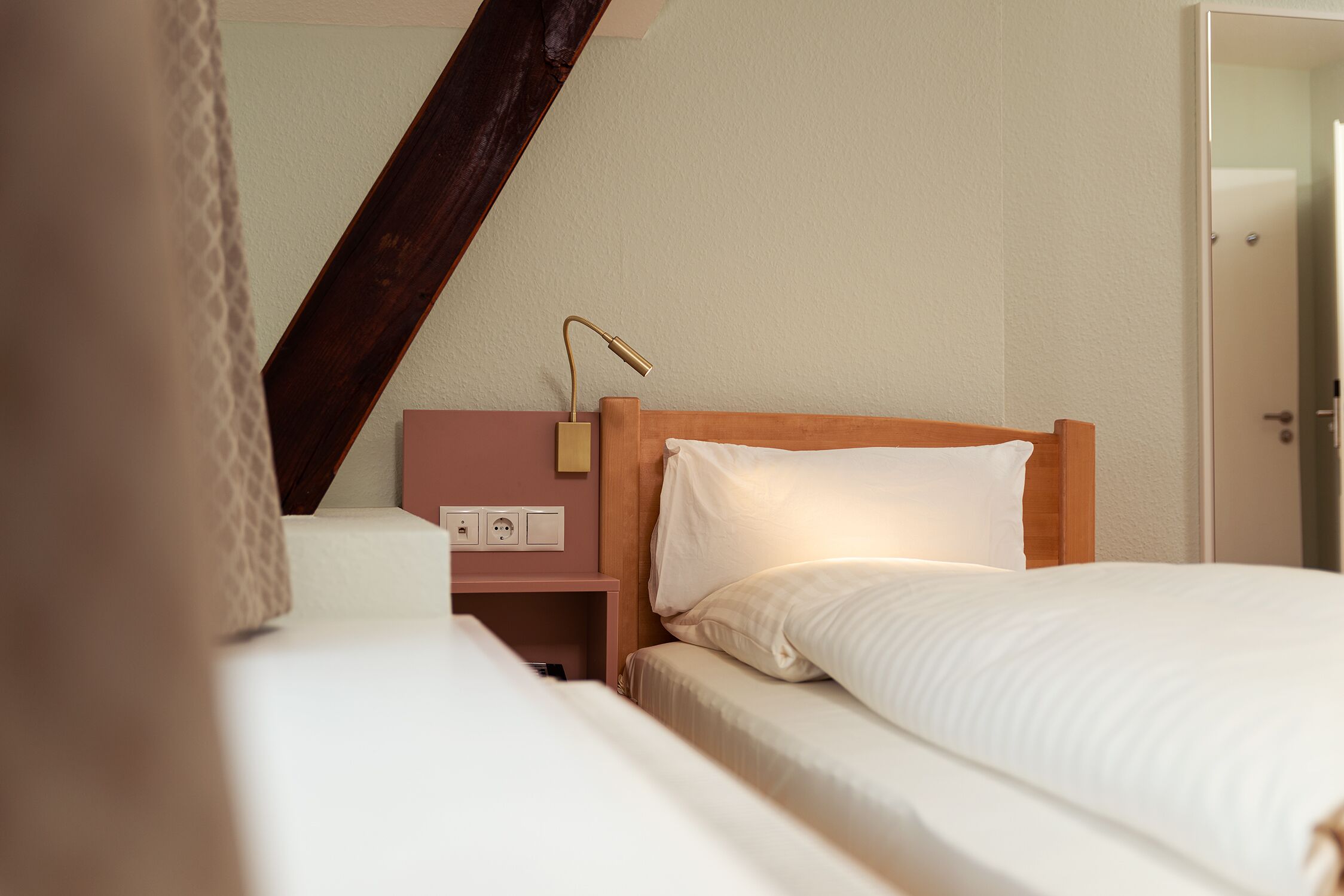 A hotel room with a wooden headboard, a bedside table with a lamp, and a power outlet.