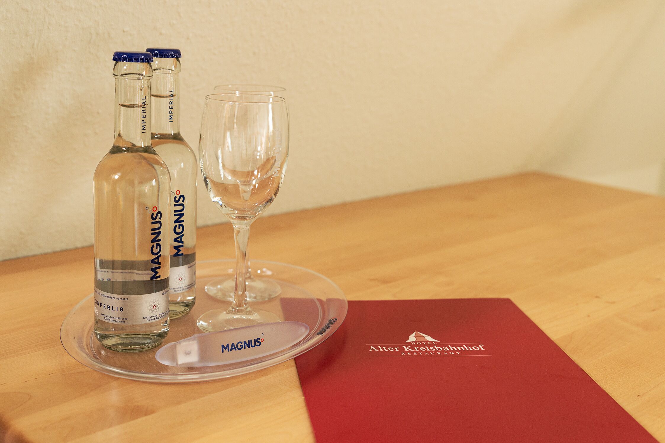 Zwei Flaschen Magnus Wein und ein Glas auf einem Holztisch mit einer roten Speisekarte.
