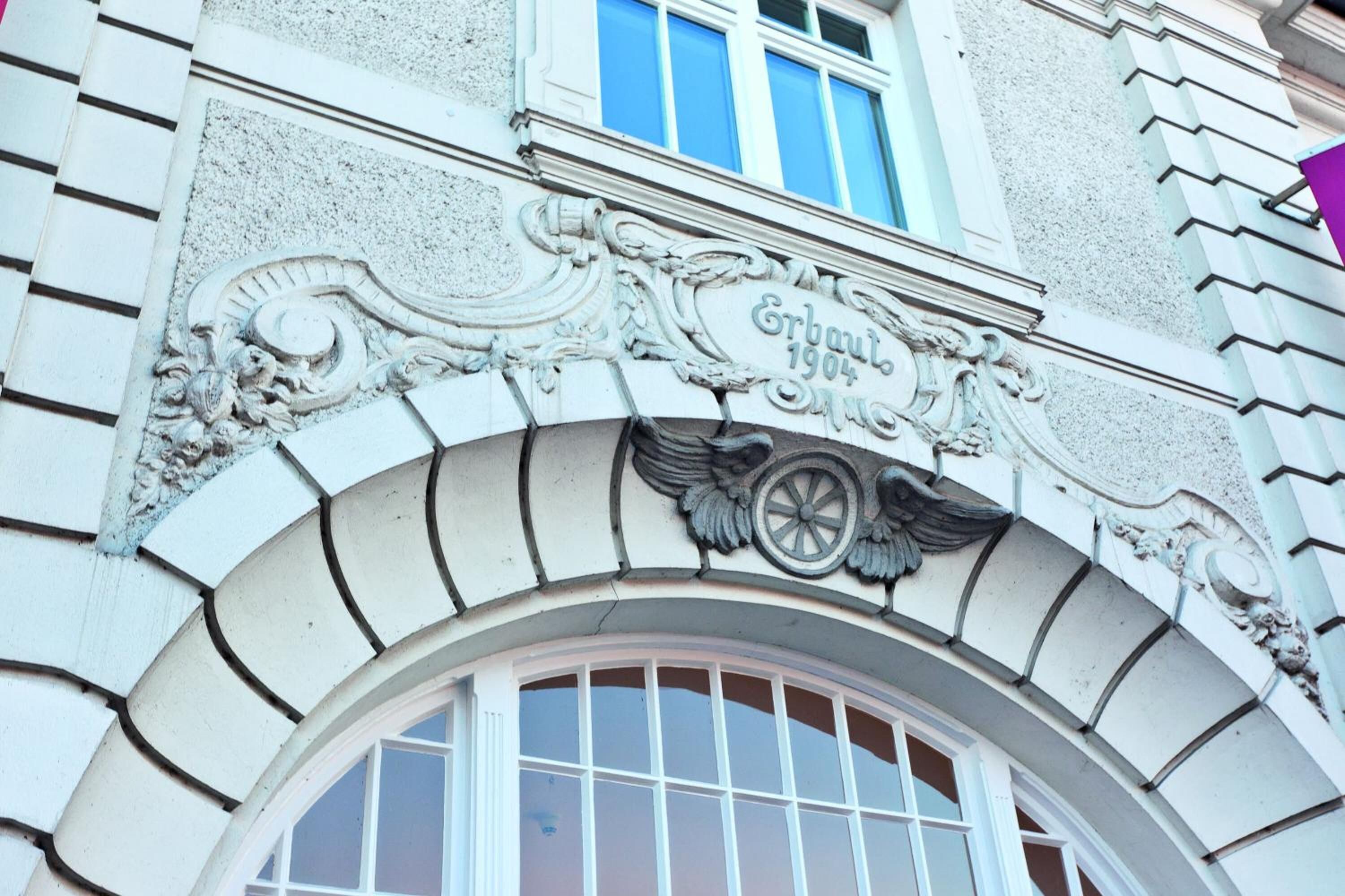 A building facade with ornate architectural details, including a decorative archway and a sign that reads "Erbau 1904."