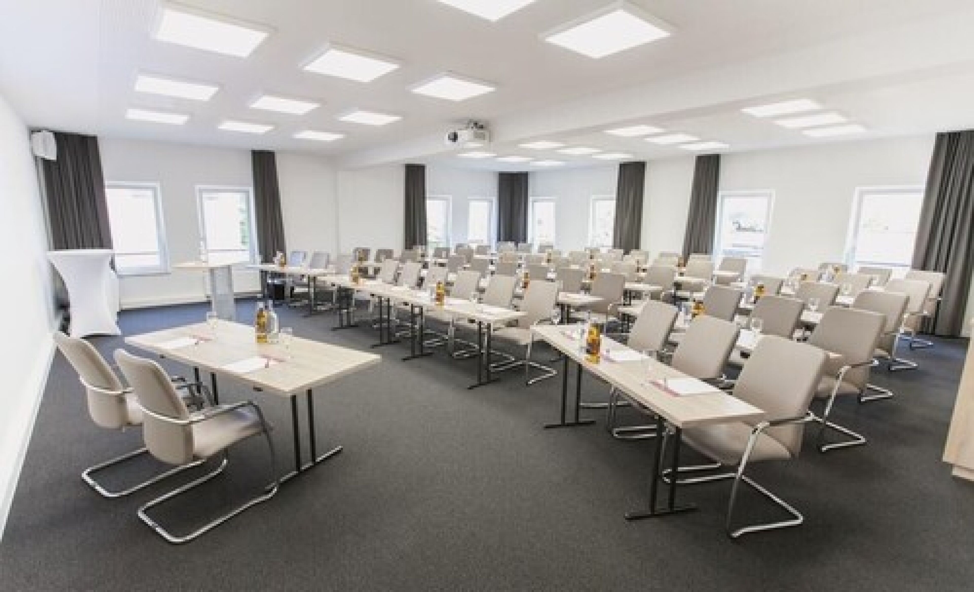 Una sala de conferències amb diverses taules i cadires, un projector i un gran finestral.