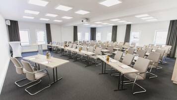 Una sala de conferències amb diverses taules i cadires, un projector i un gran finestral.