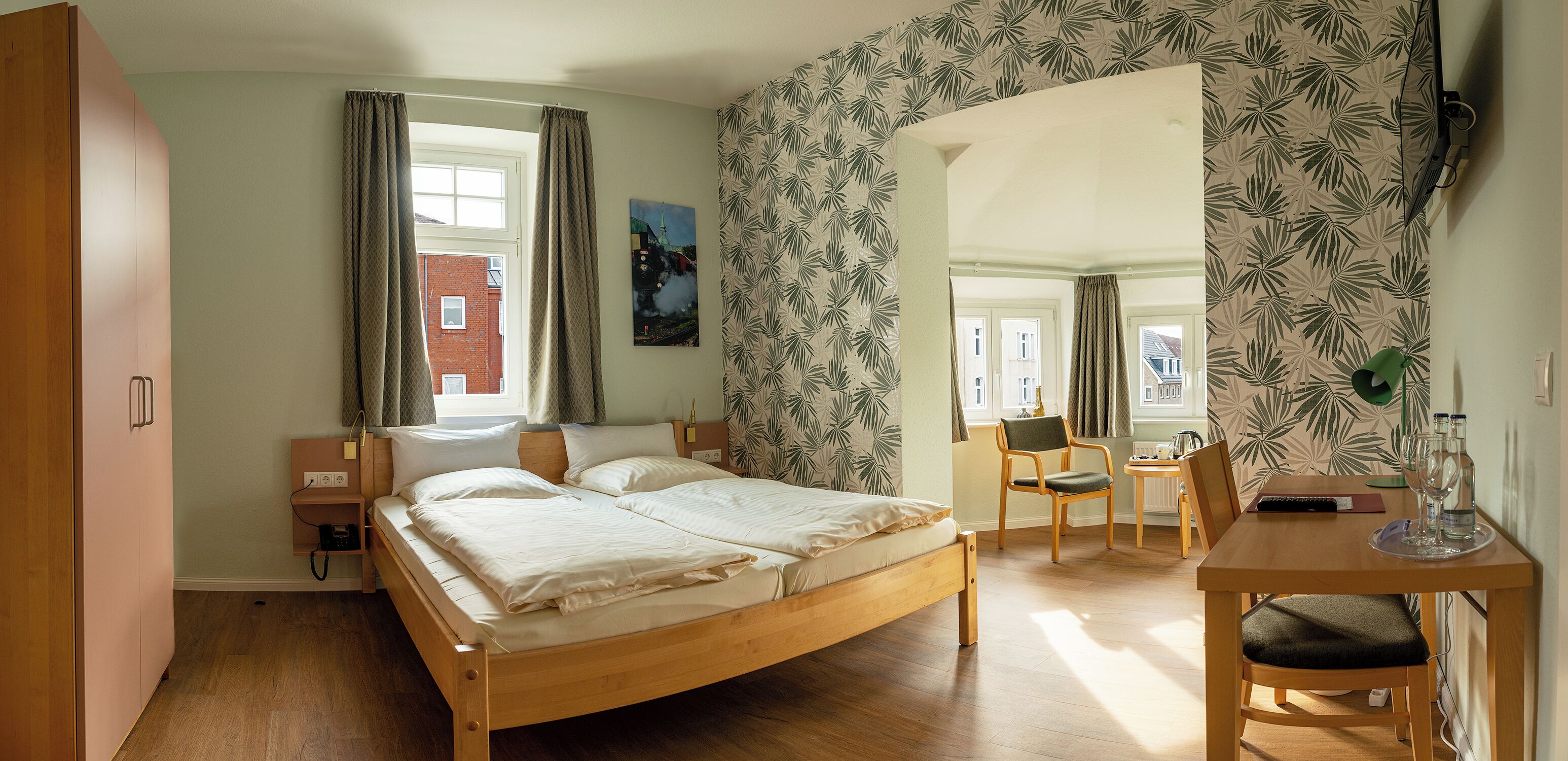 Une chambre à coucher avec un lit en bois, un bureau avec une chaise, une petite table et une fenêtre avec des rideaux.
