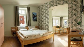 Une chambre à coucher avec un lit en bois, un bureau avec une chaise, une petite table et une fenêtre avec des rideaux.
